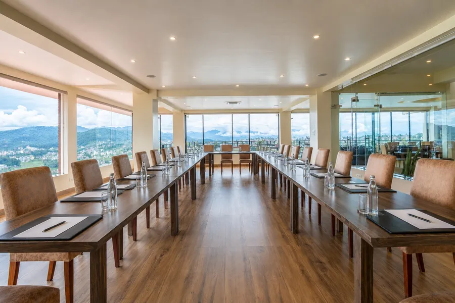 Maple Hall set in a long U-shape of about twenty-six tan leather chairs on a wooden floor, a folder, pen and water at every place, floor-to-ceiling glass on two sides looking over the valley to the hills