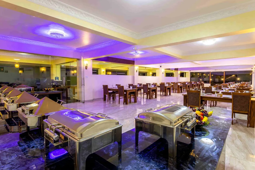 The restaurant under violet ceiling light: timber tables on a marble floor, a buffet line of chafing dishes in the foreground