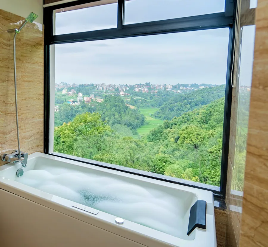 The jacuzzi tub set against a full-height window, green hills filling the glass