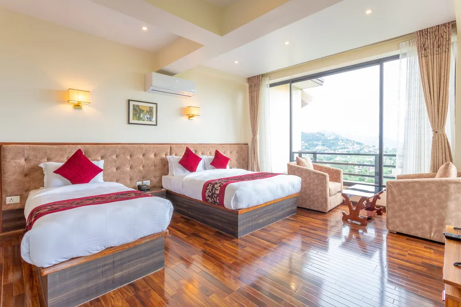 A bed with deep-red cushions beside a wide sunlit window onto the valley, a wooden chair at its foot on gleaming dark boards
