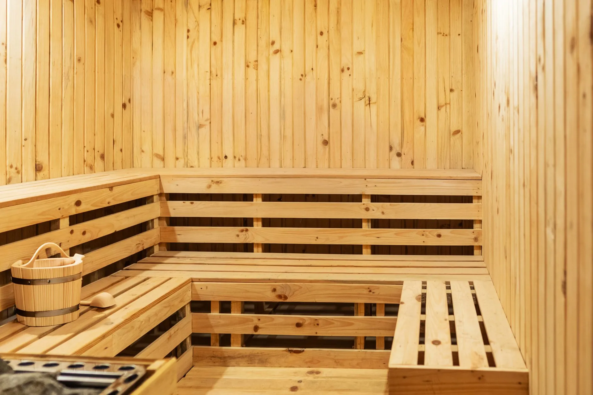 The pine-lined sauna, tiered slatted benches wrapping the corner, a wooden bucket and ladle set beside the heater