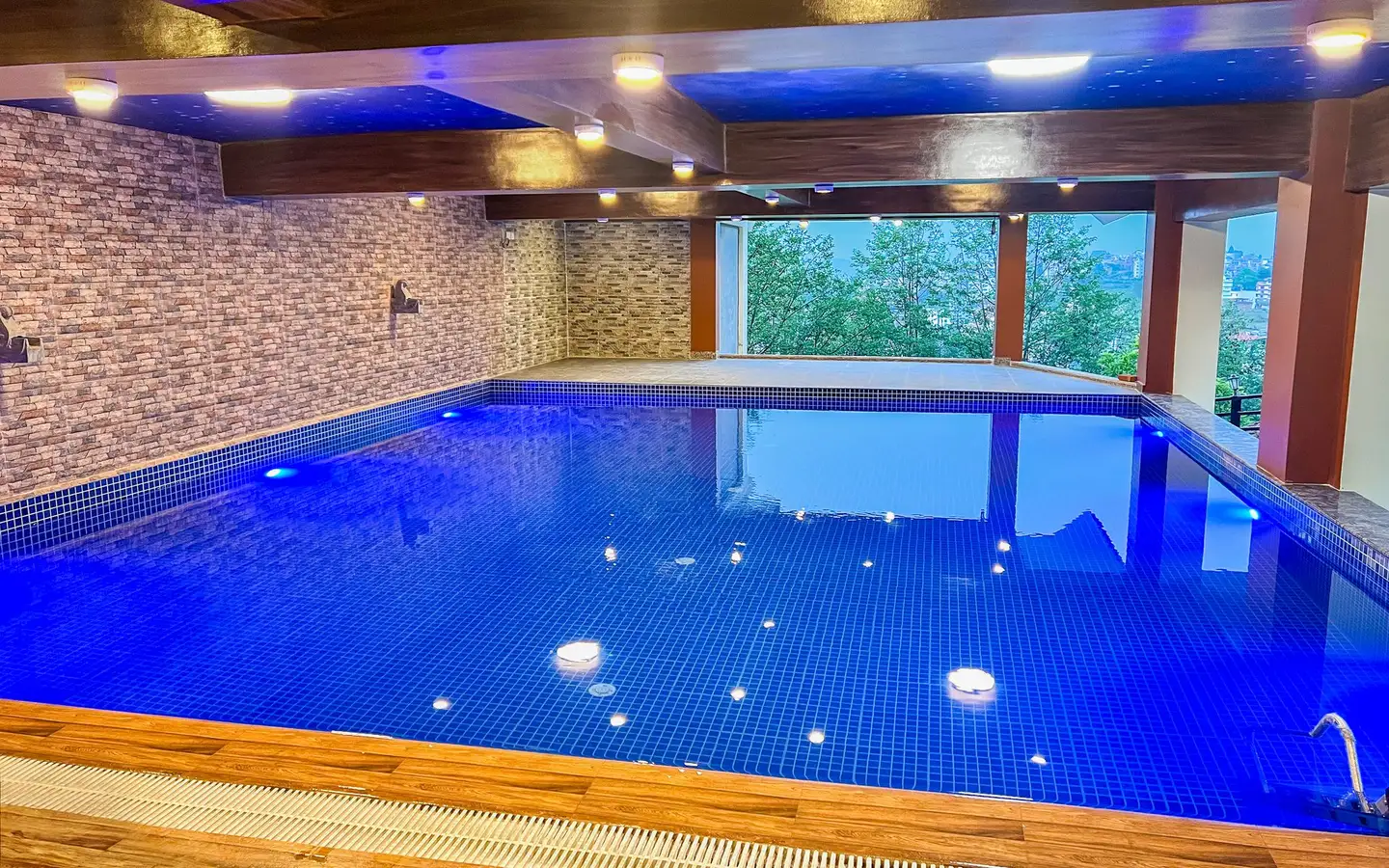 The indoor pool: blue-tiled water under a beamed ceiling, picture windows onto the trees