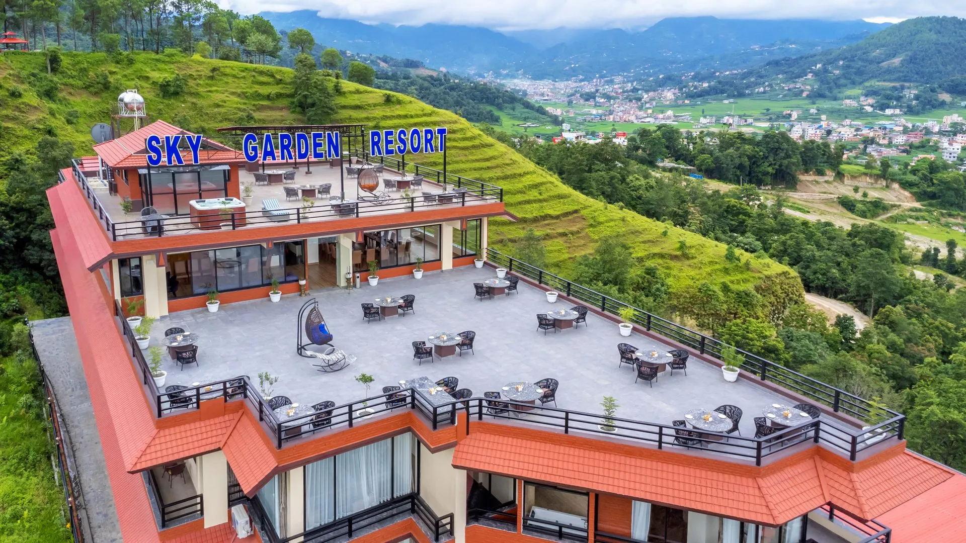The resort's stepped terraces in morning light, the SKY GARDEN RESORT sign above, green hillside and pine forest falling away to the valley