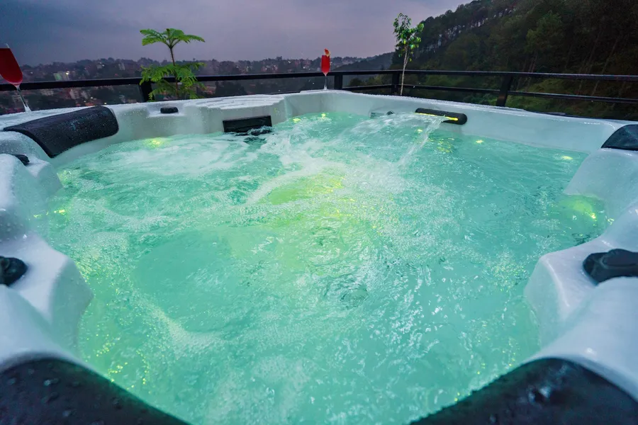 The outdoor jacuzzi at dusk, jets running and underwater lights glowing green, the valley beyond the terrace rail