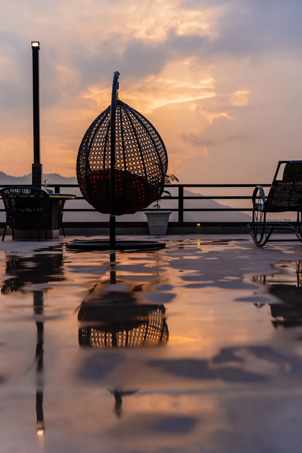 A hanging egg chair on the terrace at dusk, the hills fading beyond the rail