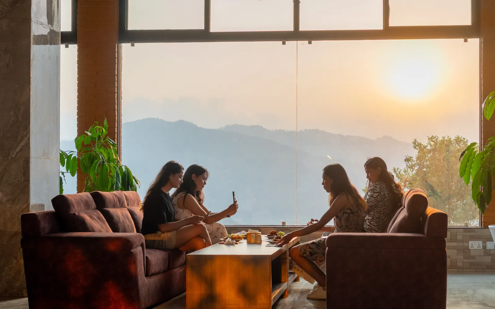 The lounge at sunset, guests by the window wall as the sun goes down over the far range