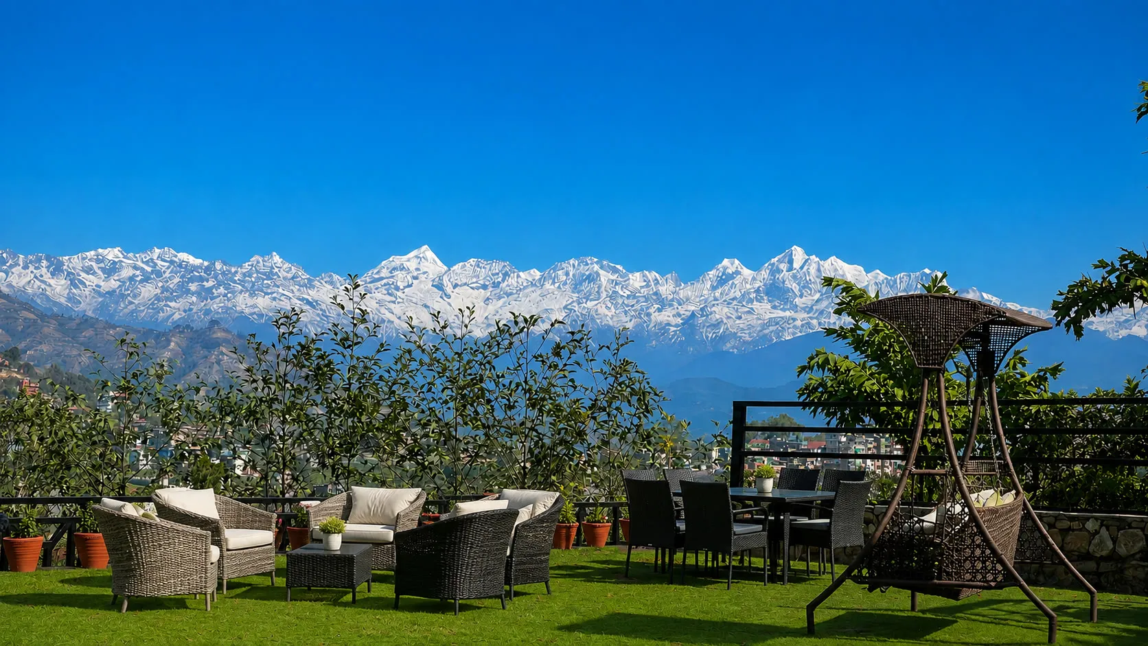 The snow line of the Himalayan range filling the horizon above the garden lawn, wicker chairs and a swing seat under a deep blue sky