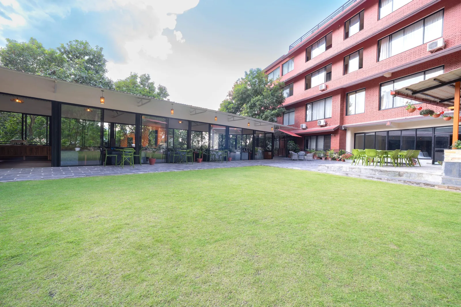 The open lawn between The Nest's long glass pavilion and the red brick wing of the resort, green cafe chairs set out along both terraces