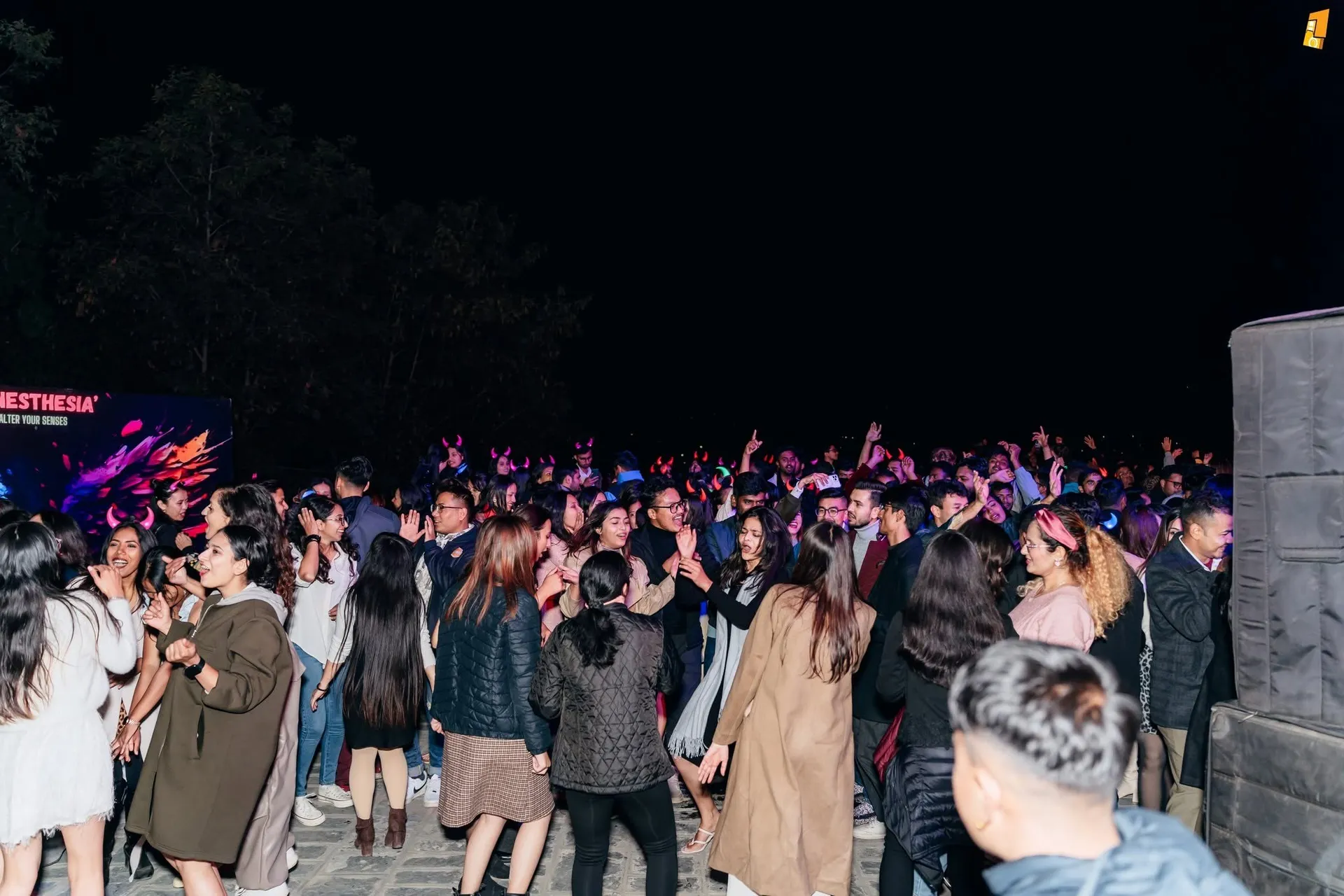 A crowd filling the open terrace after dark, hands in the air under the night sky
