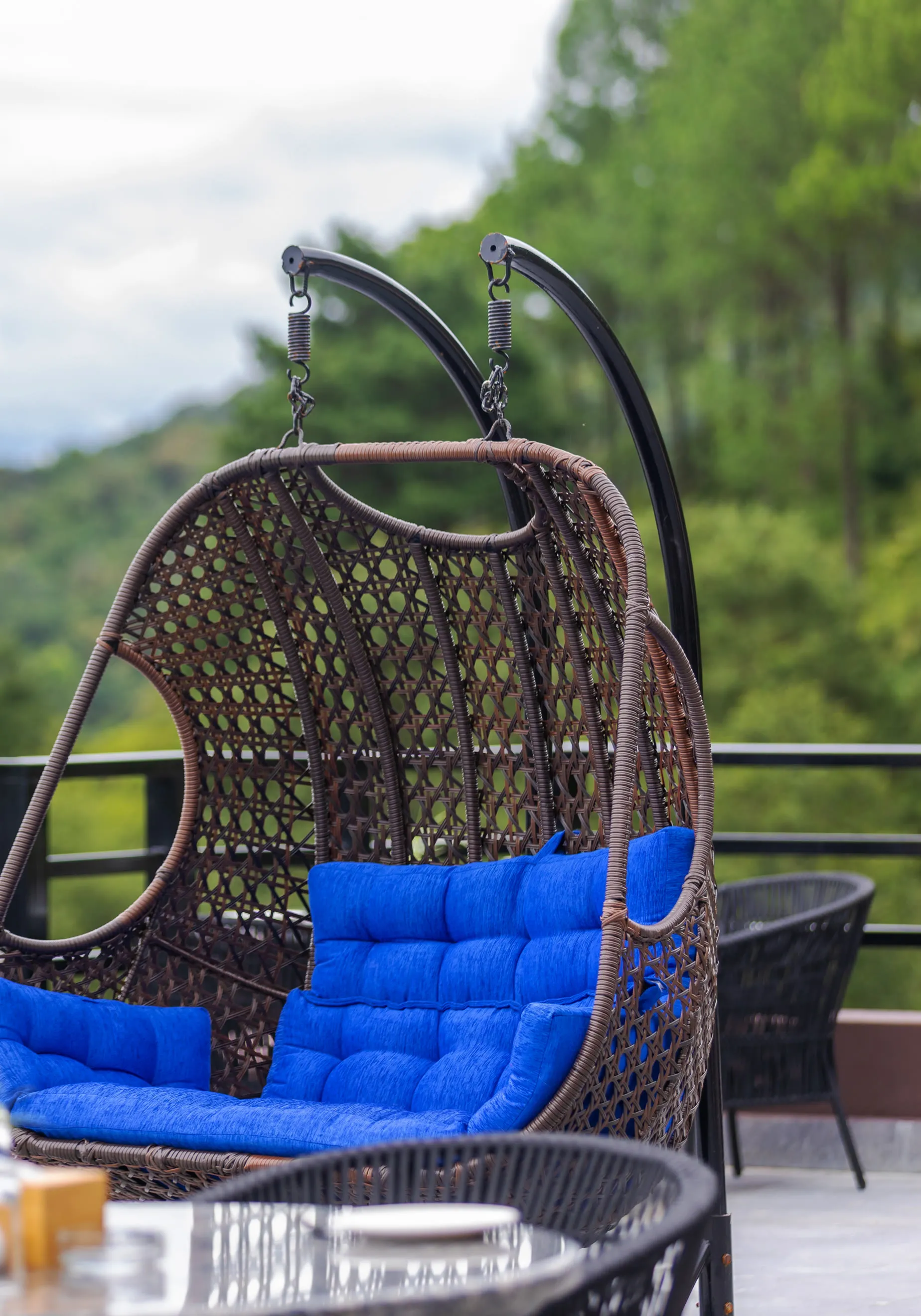 The double swing chair with royal-blue cushions on the terrace rail, loungers behind and the forested hillside beyond