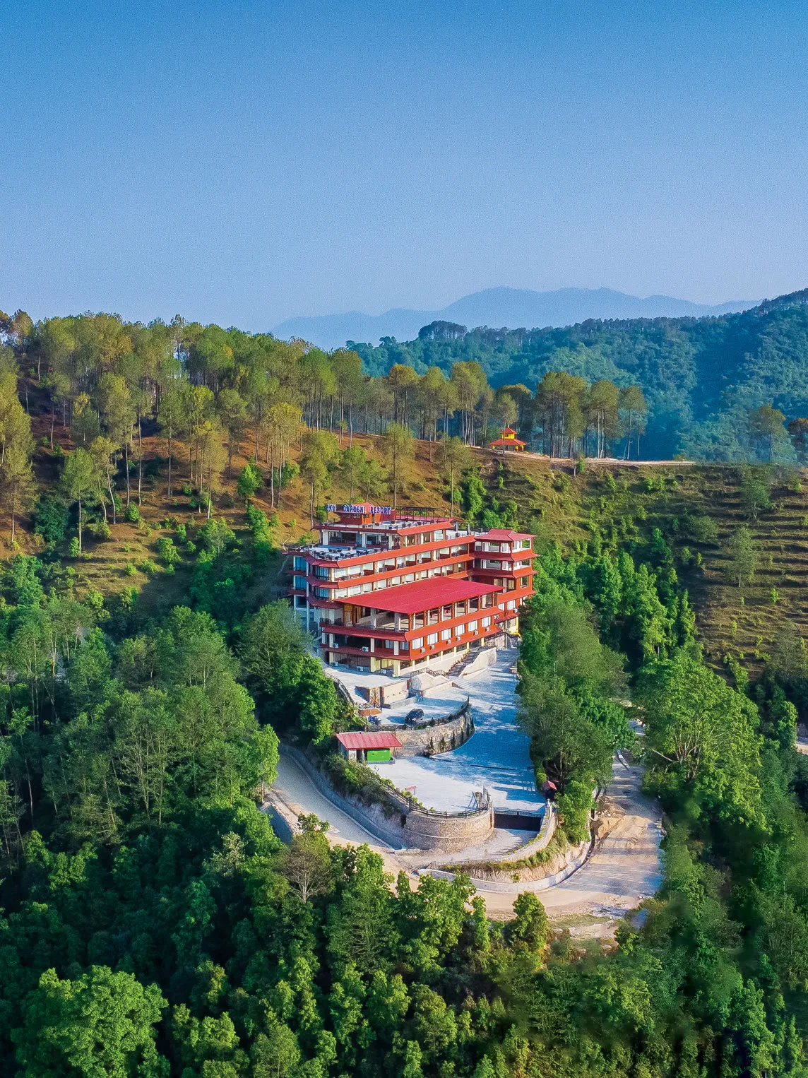 The resort on its ridge from the air, red roofs in the forest under a clear sky