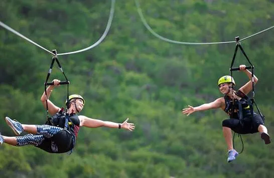 Two riders on the Dhulikhel zipline, arms out over the forested valley